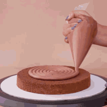 a person is frosting a cake with chocolate frosting on a cake stand .
