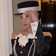 a woman wearing a top hat and pearls adjusts her pearl necklace