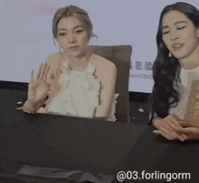 two women are sitting at a table with chinese writing on the wall in the background