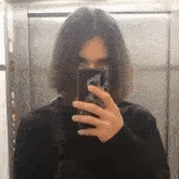 a person is taking a picture of themselves in an elevator with their phone .