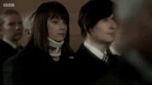 a woman with a collar around her neck stands in front of a group of people with bbc written on the bottom