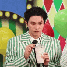 a man in a green and white striped suit and tie is holding a straw and drinking from a plastic cup .