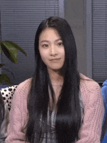 a girl with long black hair wearing a pink sweater