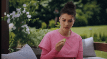 a woman in a pink shirt is eating a cucumber outside .