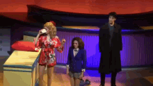 a man in a black coat is standing next to two women on a stage