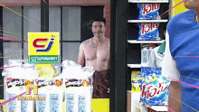 a shirtless man stands in front of a supermarket sign
