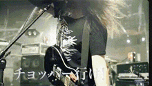 a man is playing a guitar in front of a microphone with chinese writing on the wall behind him