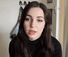 a woman wearing a black turtleneck looks at the camera with her mouth open