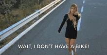 a woman in a black dress is walking down a road with the words wait , i don 't have a bike .