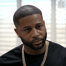 a man with a beard is wearing a black shirt and gold chain