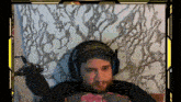 a man with a beard is wearing headphones and holding a microphone while sitting on a bed