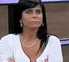 a woman wearing a white sweater and a necklace is sitting in a chair with her arms crossed .