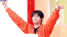 a young man in an orange jacket giving a thumbs up