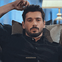 a man with a beard is sitting on a couch with his arm outstretched .