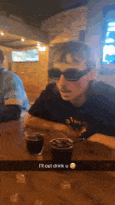 a man wearing sunglasses and a mustache is sitting at a table with a glass of beer .