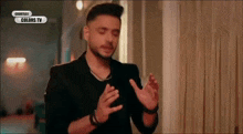 a man in a black suit is standing in front of a window with his hands outstretched .