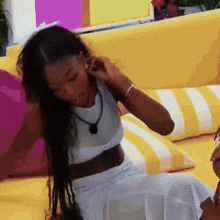 a woman is sitting on a yellow couch wearing a white crop top and white skirt .