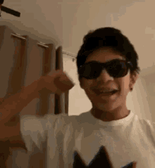 a young boy wearing sunglasses and a white shirt is standing in a room .