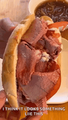 a close up of a person holding a roast beef sandwich with tomatoes and cheese .