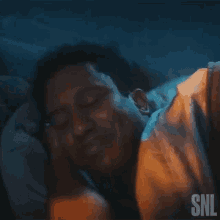 a man is sleeping in a bed with his eyes closed and smiling at the camera .