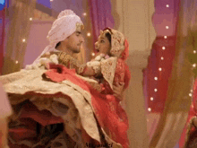 a man in a turban is carrying a woman in a red dress in his arms .