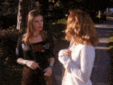 two women standing next to each other on a sidewalk talking