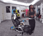 a woman in a black tank top is standing next to a chair in a room