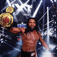 a shirtless wrestler is holding a wrestling championship belt in front of a sign that says nxt