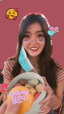 a woman wearing a mask is holding a box of macarons and a thank you card