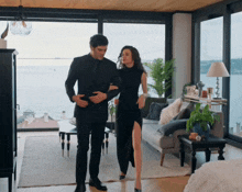 a man in a suit and a woman in a black dress are standing in a living room