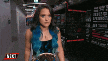 a woman with blue hair is standing in a hallway next to a sign that says " next "