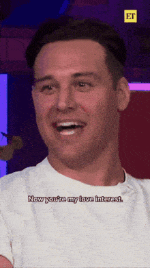 a man in a white shirt is laughing and says now you 're my love interest