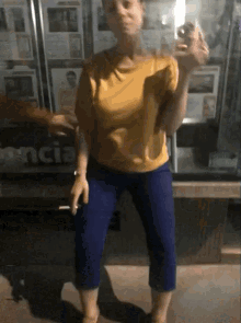 a woman in a yellow shirt is smoking a cigarette in front of a sign that says encia