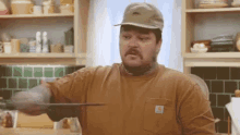 a man wearing a brown carhartt shirt is cutting something with a knife .