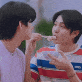 a man is feeding another man a piece of food with chopsticks while wearing a striped shirt .