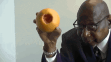 a man in a suit and tie is holding an orange with a hole in the middle