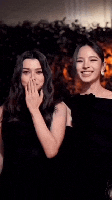 two women in black dresses are standing next to each other and smiling .