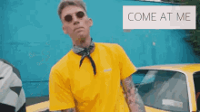 a man wearing sunglasses and a yellow shirt is standing in front of a yellow car and says come at me