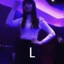 a woman is standing with her hands on her hips in front of a purple background with the letter l above her .