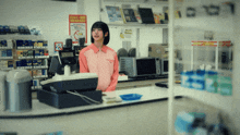 a woman stands behind a cash register in a store with a sign on the wall that says 20