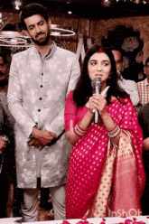a woman in a pink dress is speaking into a microphone while standing next to a man in a suit