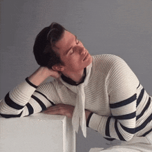 a man in a striped sweater leans on a white box with his head resting on his hand