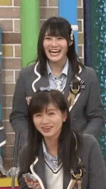 a couple of girls are laughing and smiling in front of a brick wall