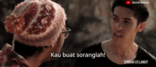 a man wearing a knitted hat talks to another man with the words kau buat soranglah on his chest