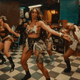 a group of women are dancing on a checkered floor in front of speakers