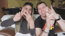 two men are making a peace sign with their hands and smiling