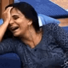 a woman is sitting on a blue couch with her hand on her face .