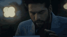 a man with a beard is holding a piece of paper in his hand in a dark room .