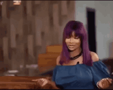 a woman with purple hair and a blue top is sitting on a couch .