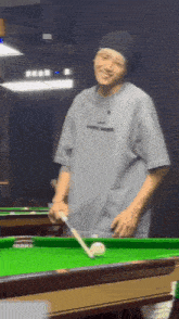 a man is standing next to a pool table holding a pool cue and smiling .